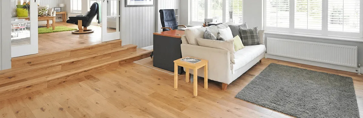 A modern living room with professionally installed laminate flooring, a beige sofa, a small side table, a gray rug, and large windows with white shutters in Chicago, IL